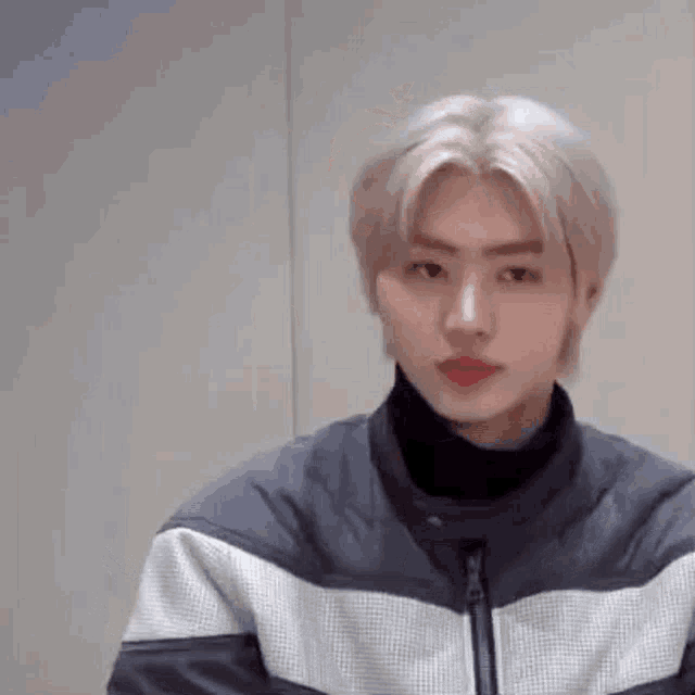 a young man with blonde hair is wearing a black turtleneck and a black jacket .