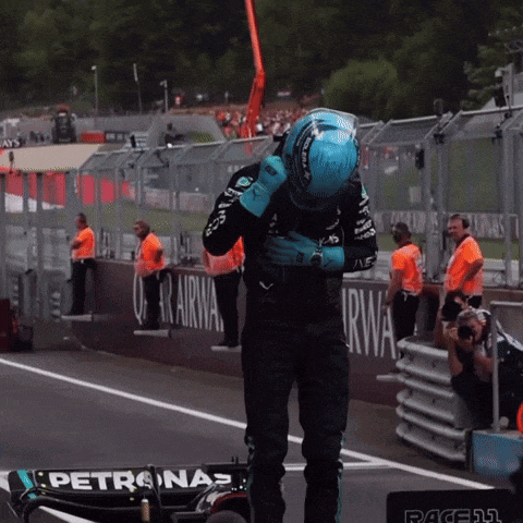 a man wearing a blue helmet is standing next to a petronas race car