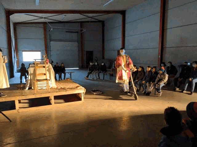 a group of people are gathered in a dark room watching a man on stilts perform