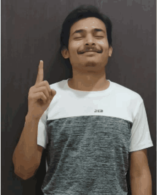 a man wearing a gray and white t-shirt is pointing up with his fingers