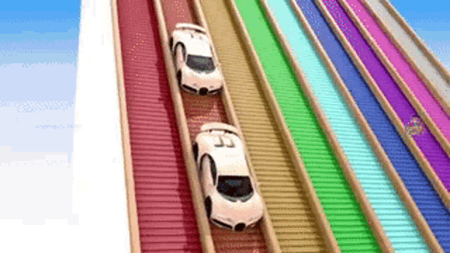 two toy cars are driving down a rainbow colored roller coaster .