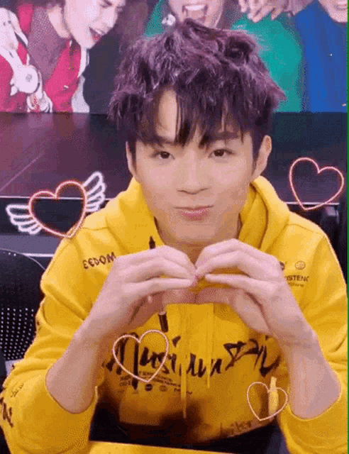 a young boy in a yellow hoodie is making a heart shape with his hands .