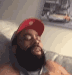 a man with a beard is laying on a bed wearing a red hat .