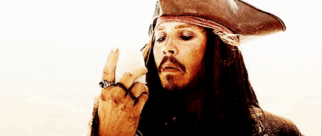 a man with dreadlocks is wearing a pirate hat and making a middle finger sign