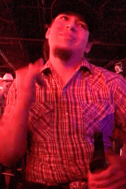 a man wearing a plaid shirt and cowboy hat is holding a beer