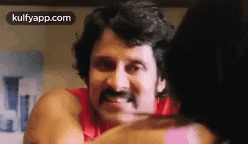 a man with a mustache is hugging a woman in a red shirt .