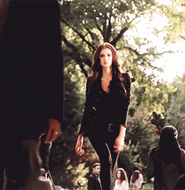a woman in a black jacket and black pants walks in a park