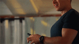 a man in a blue shirt is smiling while holding a cell phone in his hand .
