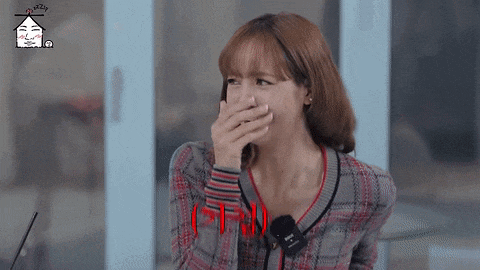 a woman is covering her mouth with her hand while wearing a plaid sweater .