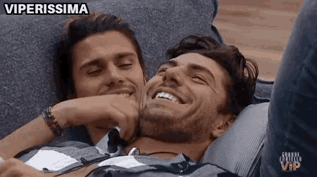 two men are laying on a couch and smiling .
