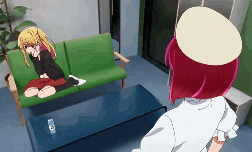 a girl sitting on a green couch next to a table with a bottle of water on it