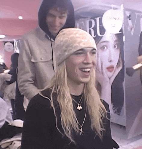 a woman with long blonde hair is smiling in front of a sign that says " ru "