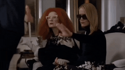 two women are sitting on a couch wearing sunglasses and a scarf .