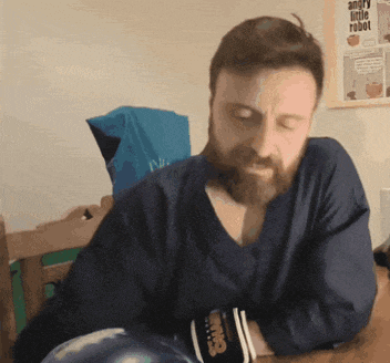 a man with a beard is sitting at a table with boxing gloves and a poster that says angry little robot