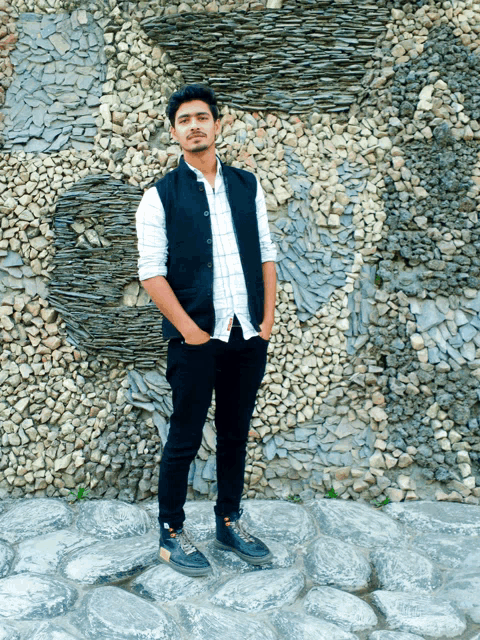 a young man standing in front of a wall of rocks
