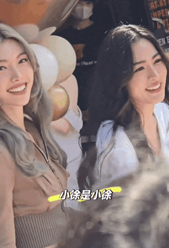 two women are smiling in front of balloons and a sign that says ' at ' on it