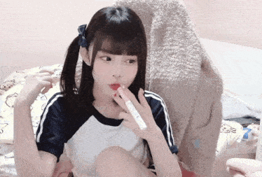 a girl with pigtails is sitting on a bed holding a bottle of lotion