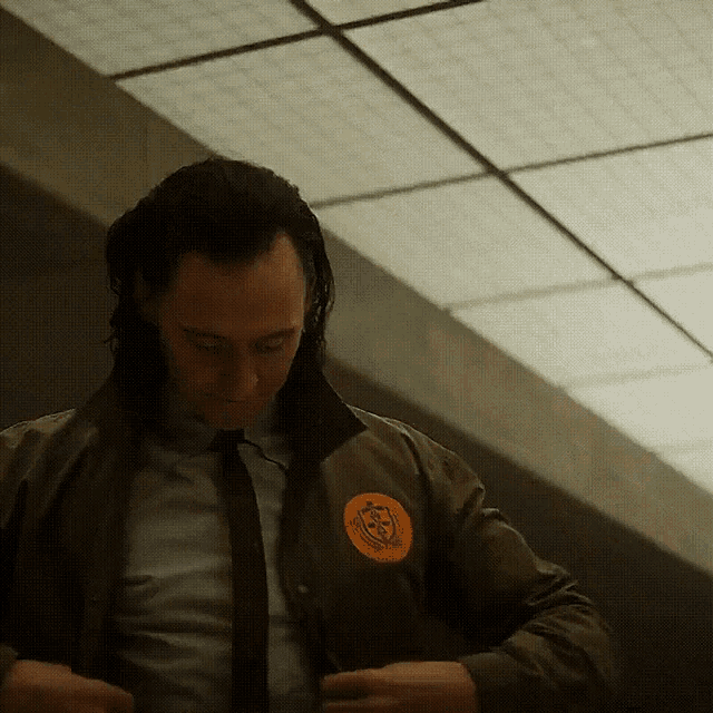 a man wearing a jacket and tie has a patch on his jacket that says ' loki '