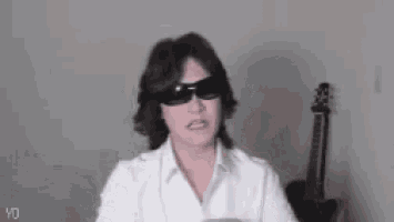 a person wearing sunglasses and a white shirt is making a heart shape with their hands .