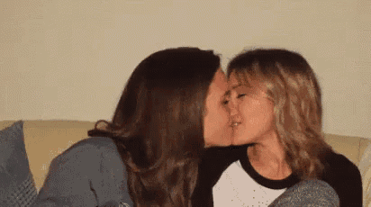 two women are kissing on a couch .