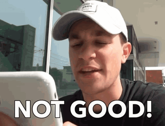 a man wearing a white hat is looking at his phone and says " not good "