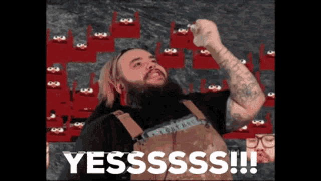a man with a beard is standing in front of red chairs and says " yesssss "