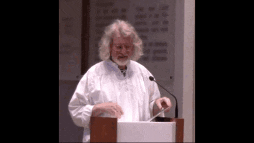 a man in a white robe stands at a podium with a microphone in front of him