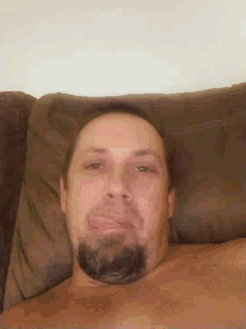 a shirtless man with a beard is laying on a brown couch