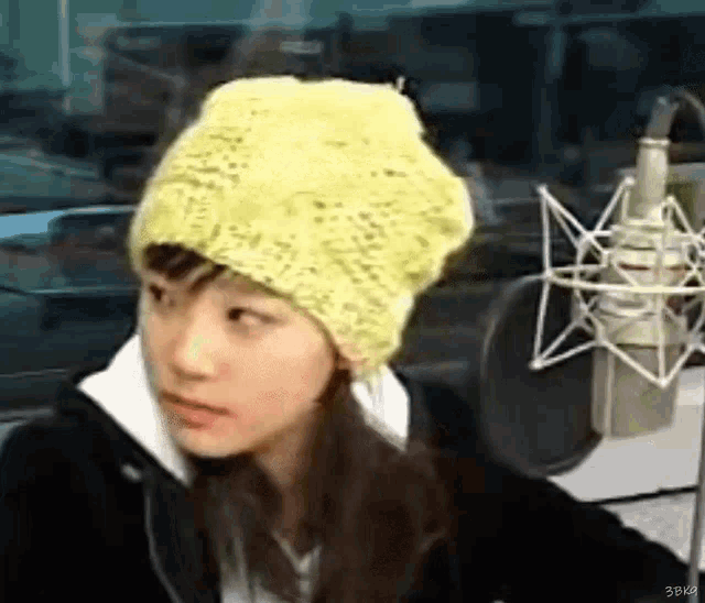 a young girl wearing a yellow hat is sitting in front of a microphone .