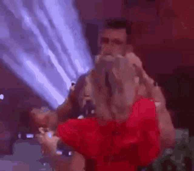 a man is holding a woman in his arms while she sings into a microphone at a concert .