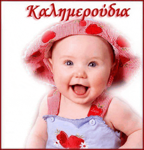 a baby wearing a hat and overalls with strawberries on it is smiling .