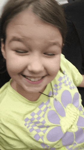 a young girl wearing a purple and yellow shirt smiles