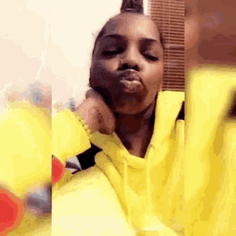 a woman in a yellow hoodie is blowing a kiss while taking a selfie .