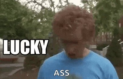 a man wearing a wig and sunglasses is saying `` lucky ass '' while standing in front of trees .