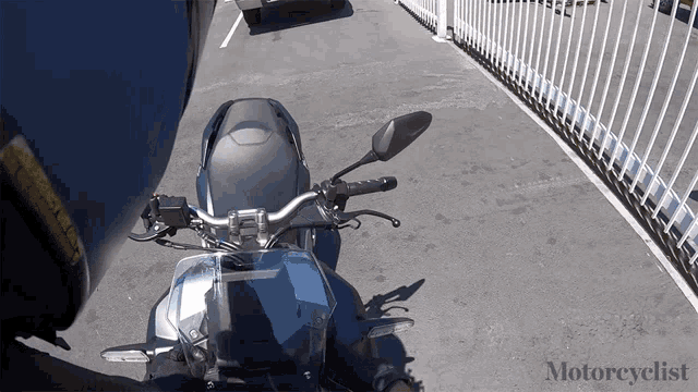 a motorcycle is parked in a parking lot next to a fence and the word motorcyclist is on the bottom of the screen
