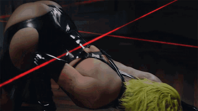 a woman in a black latex outfit is laying on her back with red lasers behind her
