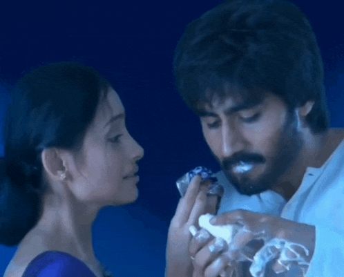 a man and a woman are looking at each other and the man is holding a piece of cake in his mouth