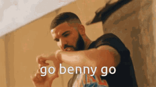 a man with a beard is standing in front of a wall and says go benny go