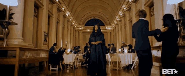 a woman in a long black dress walks through a hallway with tables and chairs and a bet logo