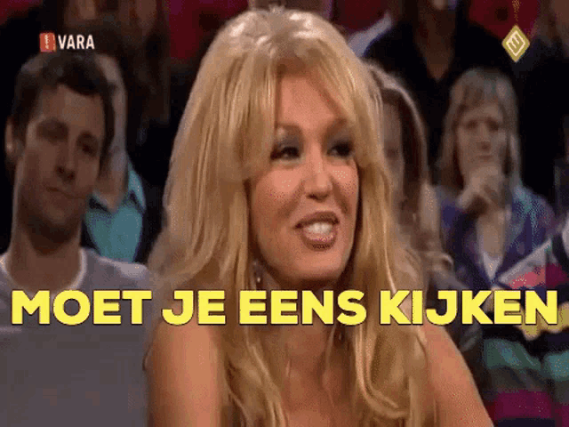 a woman sitting in front of a crowd with the words " moet je eens kijken " on the bottom