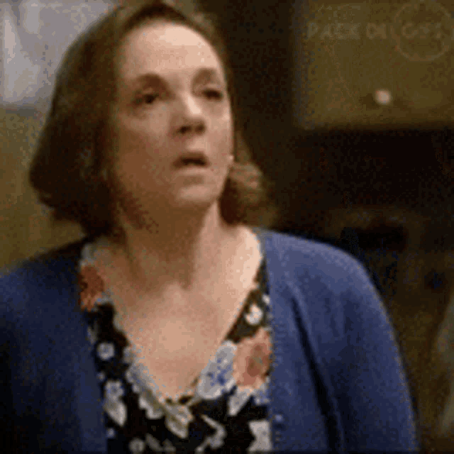 a woman wearing a blue cardigan and a floral shirt is looking at the camera .