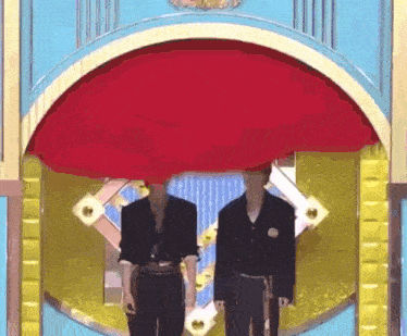 two men are standing next to each other in front of a large red curtain .
