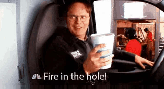 a man is sitting in a van holding a cup of coffee and saying `` fire in the hole ! ''