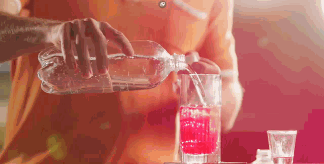 a person is pouring a drink into a glass with a red liquid in it
