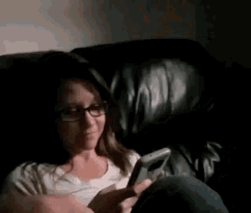 a woman with glasses is sitting on a couch looking at her phone