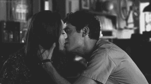 a black and white photo of a man and woman kissing in a bar .