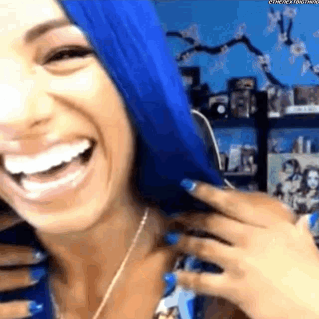 a woman with blue hair is laughing and smiling while holding her hair .