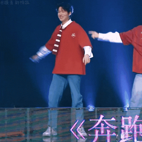 a man in a red shirt is dancing in front of a screen with chinese characters on it