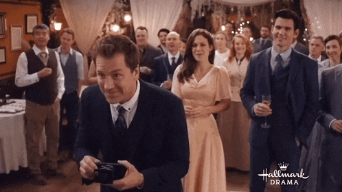a man in a suit is holding a camera in front of a group of people with the words hallmark drama on the bottom