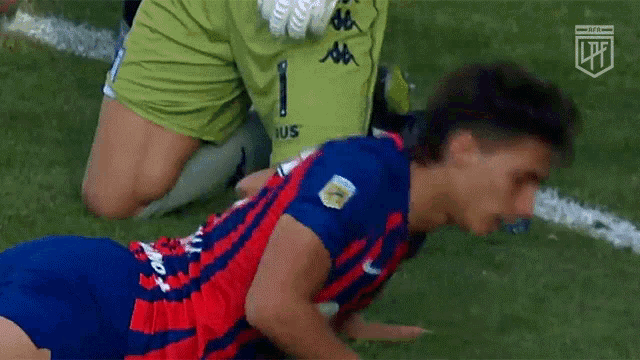 a soccer player is laying on the ground while a soccer goalie kneels over him .